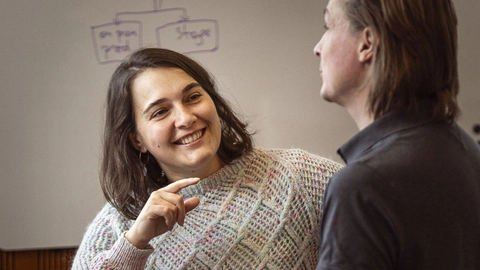 To personer i en kontorindstilling, der engagerer sig i en positiv samtale, en kvinde i en farverig sweater smiler og peger, mens en mand i en mørk skjorte lytter opmærksomt.